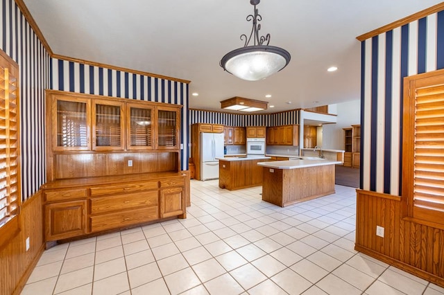 kitchen with pendant lighting, white appliances, wood walls, and a kitchen island