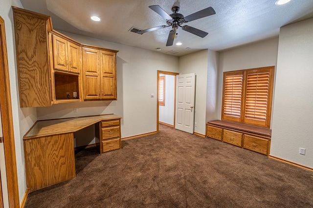 unfurnished office featuring built in desk, ceiling fan, and dark colored carpet