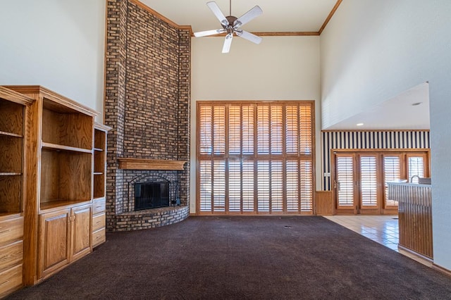 unfurnished living room with a towering ceiling, a brick fireplace, carpet floors, ornamental molding, and ceiling fan