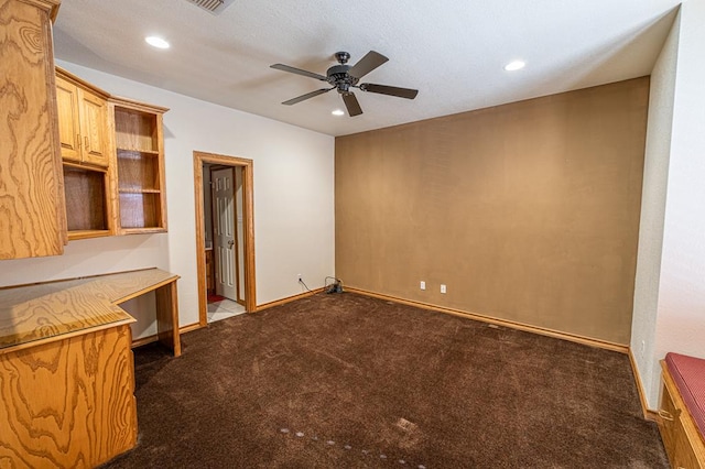 interior space featuring ceiling fan, dark carpet, and built in desk