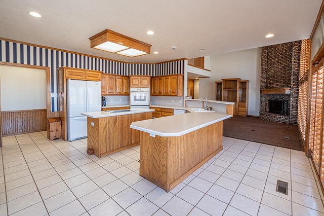 kitchen featuring kitchen peninsula, sink, white appliances, a center island, and wooden walls