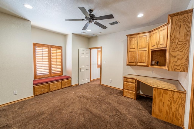 unfurnished office featuring built in desk, dark carpet, and ceiling fan