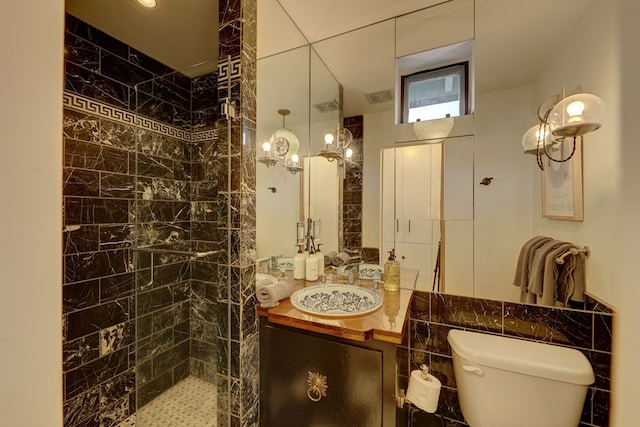 bathroom with vanity, toilet, tiled shower, and tile walls