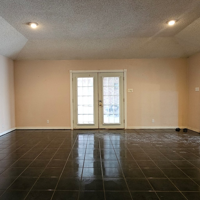 spare room with a textured ceiling, french doors, dark tile patterned flooring, and baseboards