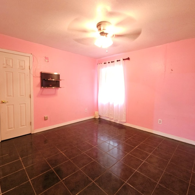 empty room featuring a ceiling fan, dark tile patterned flooring, and baseboards