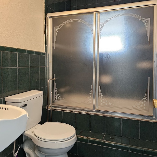 full bath with tiled shower / bath combo, a sink, toilet, and tile walls