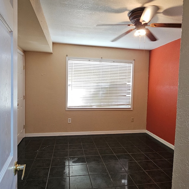 spare room with dark tile patterned floors, baseboards, and a ceiling fan