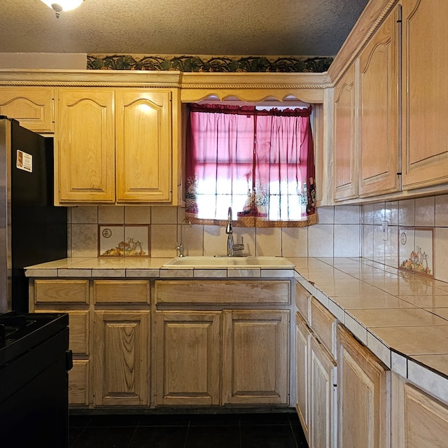 kitchen with a textured ceiling, dark tile patterned floors, a sink, tile counters, and black appliances