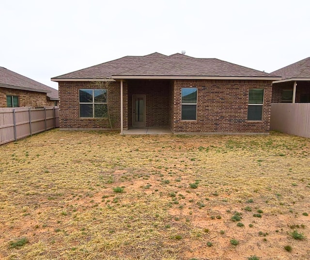 rear view of house with brick siding, a yard, a shingled roof, and a fenced backyard