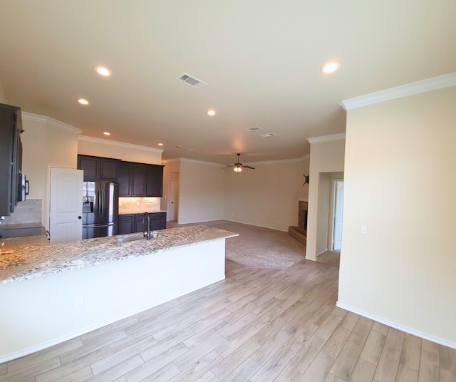 kitchen featuring a peninsula, light stone countertops, stainless steel refrigerator with ice dispenser, and a sink