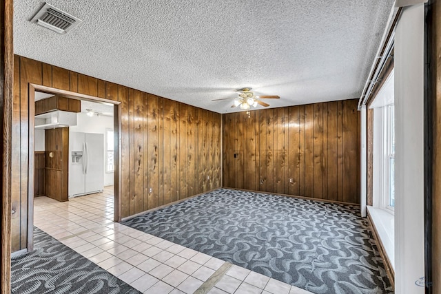 spare room featuring light tile patterned floors, plenty of natural light, wooden walls, and a textured ceiling