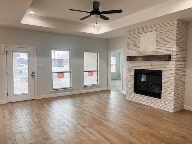 unfurnished living room featuring a ceiling fan, a tray ceiling, a fireplace, and light wood finished floors