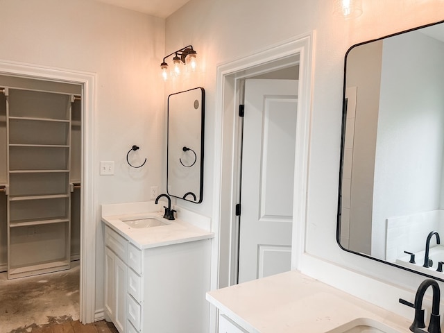 full bath featuring a walk in closet, two vanities, unfinished concrete flooring, and a sink