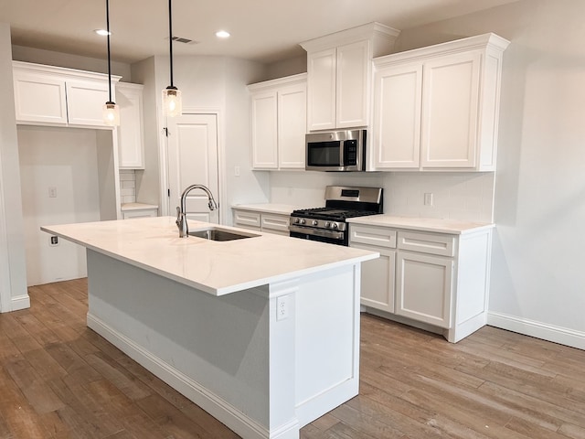 kitchen with a center island with sink, white cabinets, stainless steel appliances, light wood-type flooring, and a sink