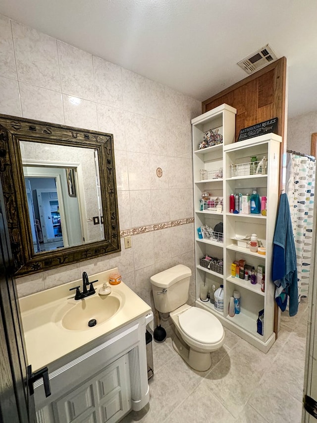 bathroom featuring tile patterned flooring, vanity, toilet, and tile walls