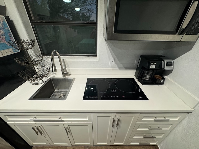 kitchen with black electric stovetop, white cabinetry, and sink