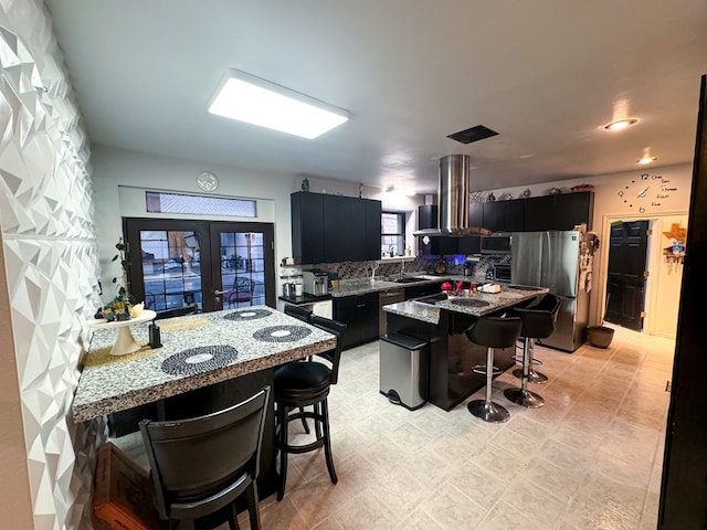 kitchen with a center island, stainless steel fridge, light stone countertops, island range hood, and a breakfast bar area