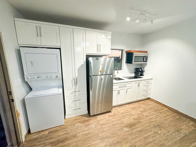 kitchen with light hardwood / wood-style flooring, white cabinets, stacked washing maching and dryer, and appliances with stainless steel finishes