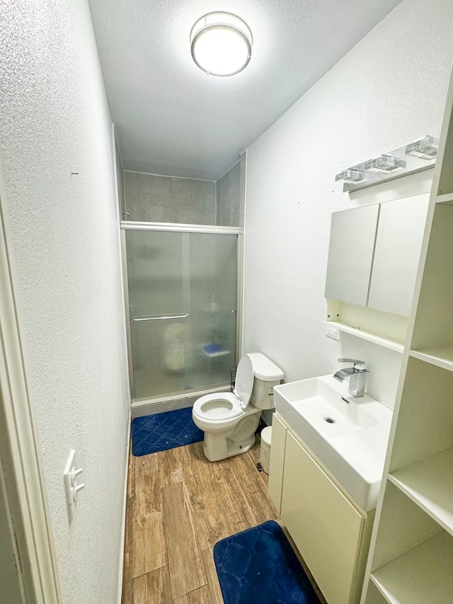 bathroom featuring vanity, hardwood / wood-style flooring, toilet, a textured ceiling, and a shower with shower door