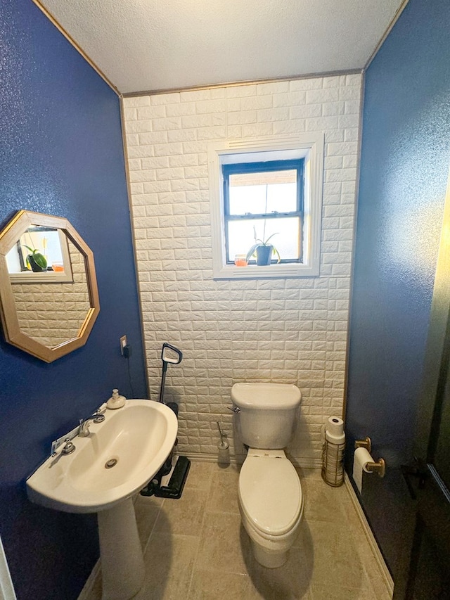 bathroom featuring tile patterned flooring, toilet, a textured ceiling, and brick wall