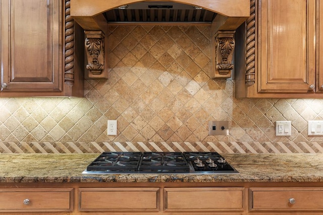 kitchen featuring stainless steel gas stovetop, ventilation hood, backsplash, and light stone counters