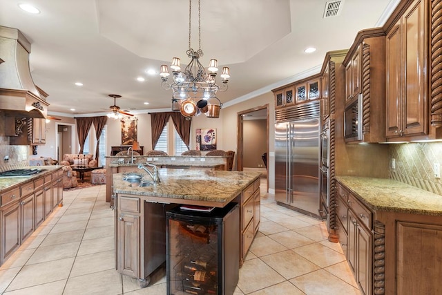 kitchen featuring ceiling fan with notable chandelier, a tray ceiling, beverage cooler, and built in appliances