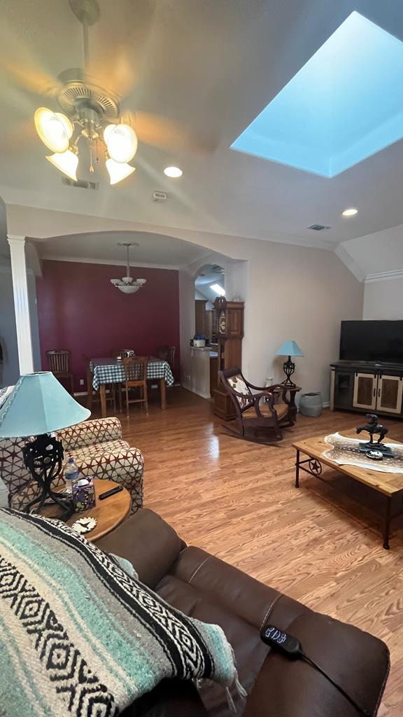 living room with ceiling fan, hardwood / wood-style floors, and vaulted ceiling with skylight