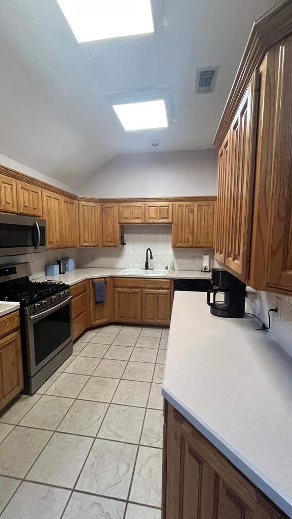 kitchen featuring backsplash, appliances with stainless steel finishes, light tile patterned floors, sink, and lofted ceiling