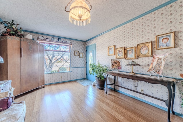 entryway with a textured ceiling, a chandelier, crown molding, and light hardwood / wood-style flooring