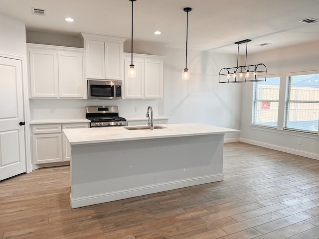 kitchen with white cabinets, sink, stainless steel appliances, and a center island with sink