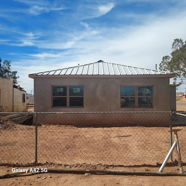 view of side of property with metal roof, fence, and stucco siding