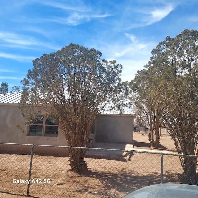 view of side of property featuring metal roof, fence, a standing seam roof, and stucco siding