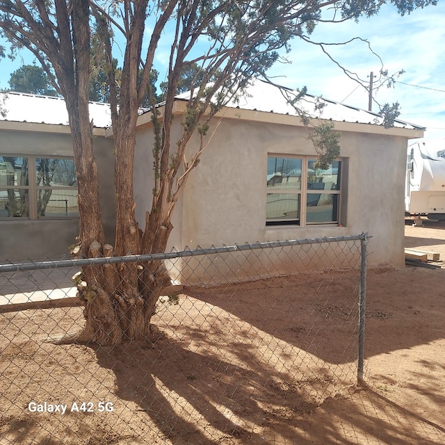 view of side of home with fence, metal roof, and stucco siding