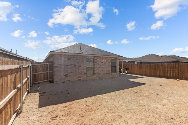 back of house with a shingled roof, a fenced backyard, and brick siding