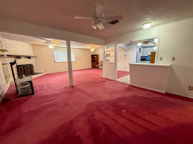 unfurnished living room with a textured ceiling, light colored carpet, and a brick fireplace