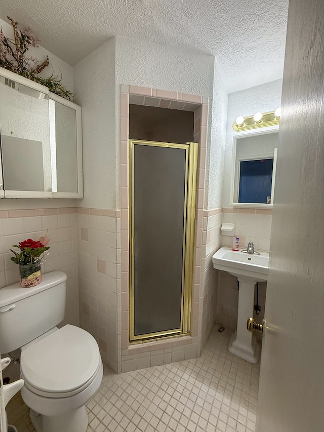 bathroom with a textured ceiling, a shower with door, sink, tile walls, and toilet