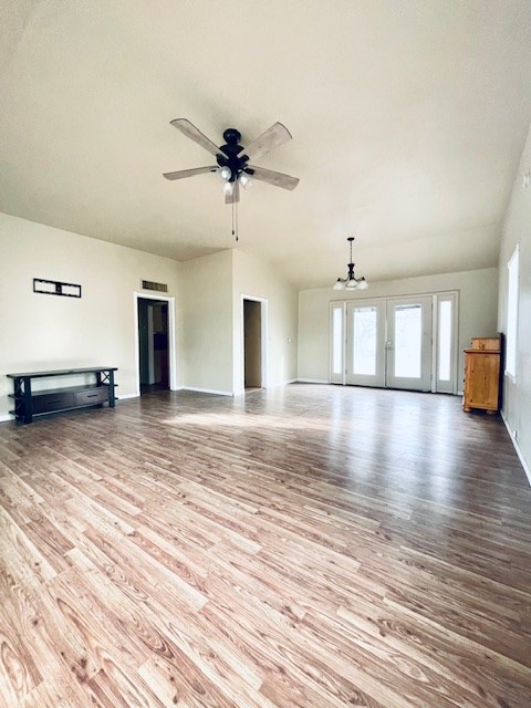 unfurnished living room featuring ceiling fan with notable chandelier and light hardwood / wood-style flooring