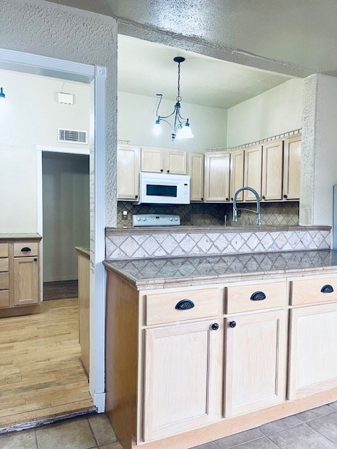 kitchen with range, decorative light fixtures, decorative backsplash, and light brown cabinets