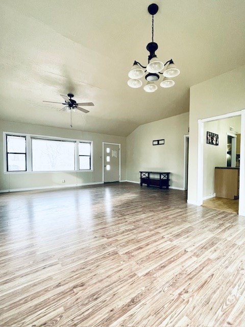 unfurnished living room featuring vaulted ceiling, ceiling fan with notable chandelier, and light hardwood / wood-style flooring