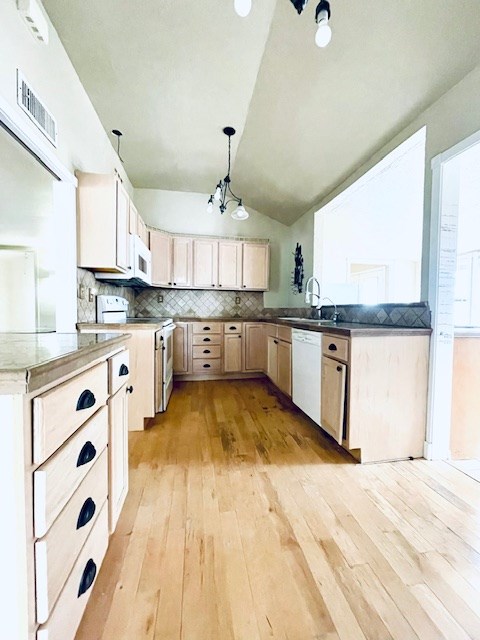 kitchen with sink, white appliances, decorative light fixtures, vaulted ceiling, and kitchen peninsula