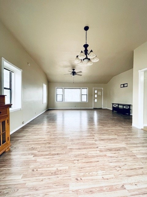 unfurnished living room with ceiling fan with notable chandelier, vaulted ceiling, light hardwood / wood-style floors, and a healthy amount of sunlight