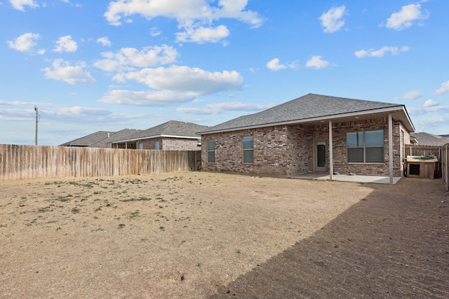 rear view of house featuring brick siding, a fenced backyard, roof with shingles, and a patio