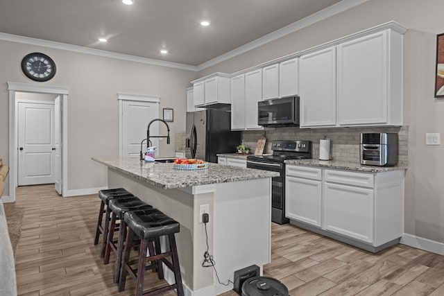 kitchen featuring black appliances, a center island with sink, light stone counters, and white cabinets