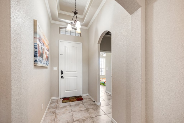 foyer entrance featuring arched walkways, light tile patterned floors, baseboards, a raised ceiling, and crown molding