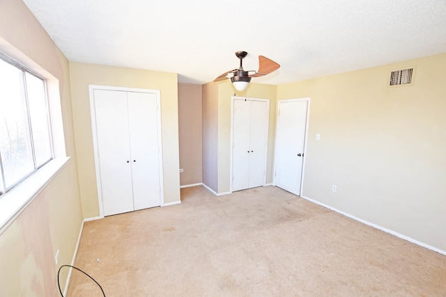 unfurnished bedroom featuring ceiling fan, a textured ceiling, light carpet, and two closets