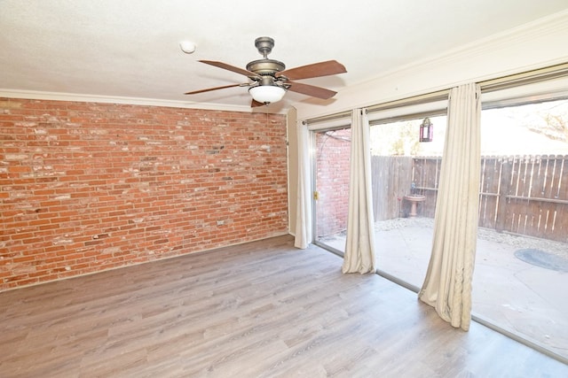 empty room featuring ceiling fan, ornamental molding, brick wall, and light wood-type flooring