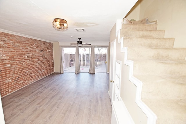 spare room with crown molding, brick wall, wood-type flooring, and ceiling fan