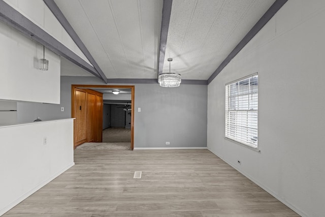 unfurnished dining area with an inviting chandelier, lofted ceiling with beams, and light hardwood / wood-style floors