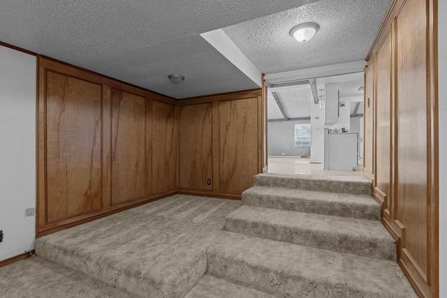 staircase featuring carpet, a textured ceiling, and wooden walls