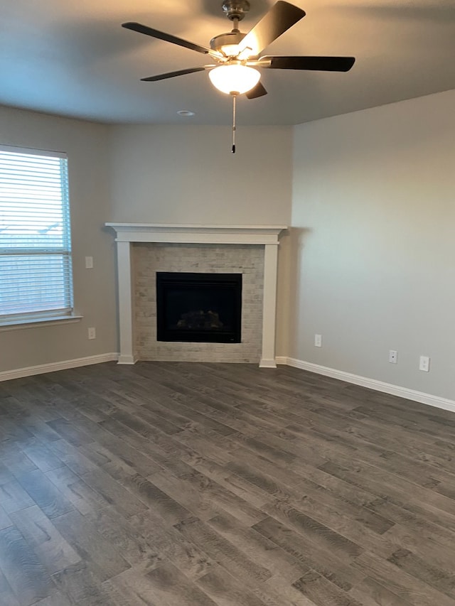 unfurnished living room featuring a tile fireplace, dark wood-style flooring, ceiling fan, and baseboards